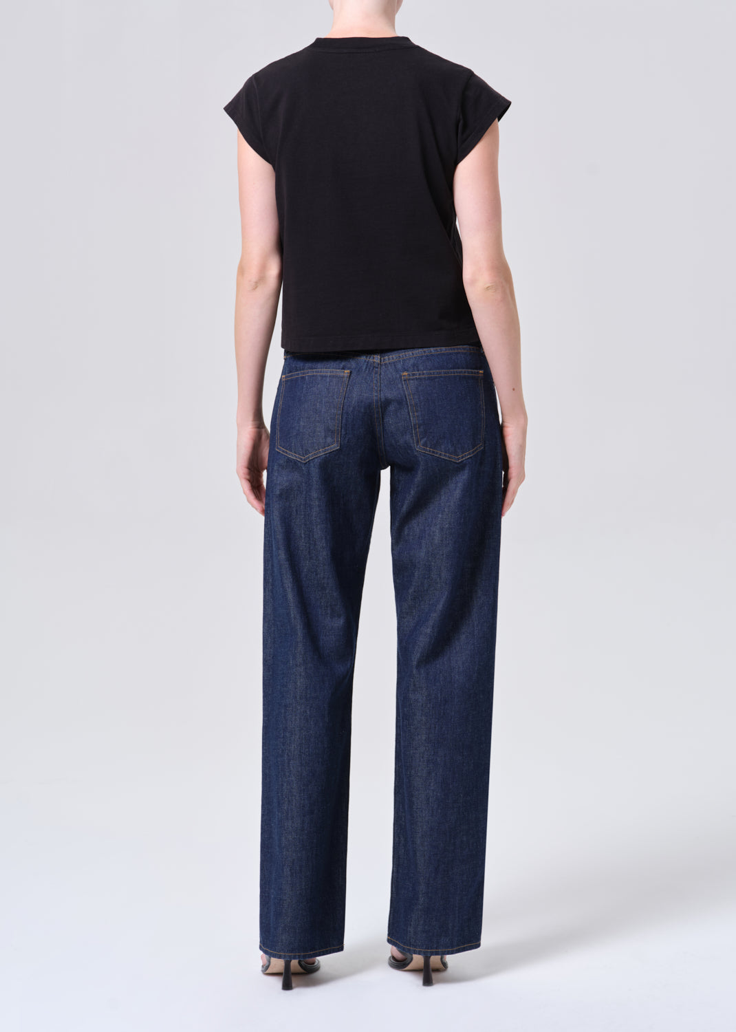 Person wearing a black top and blue jeans on a white background
