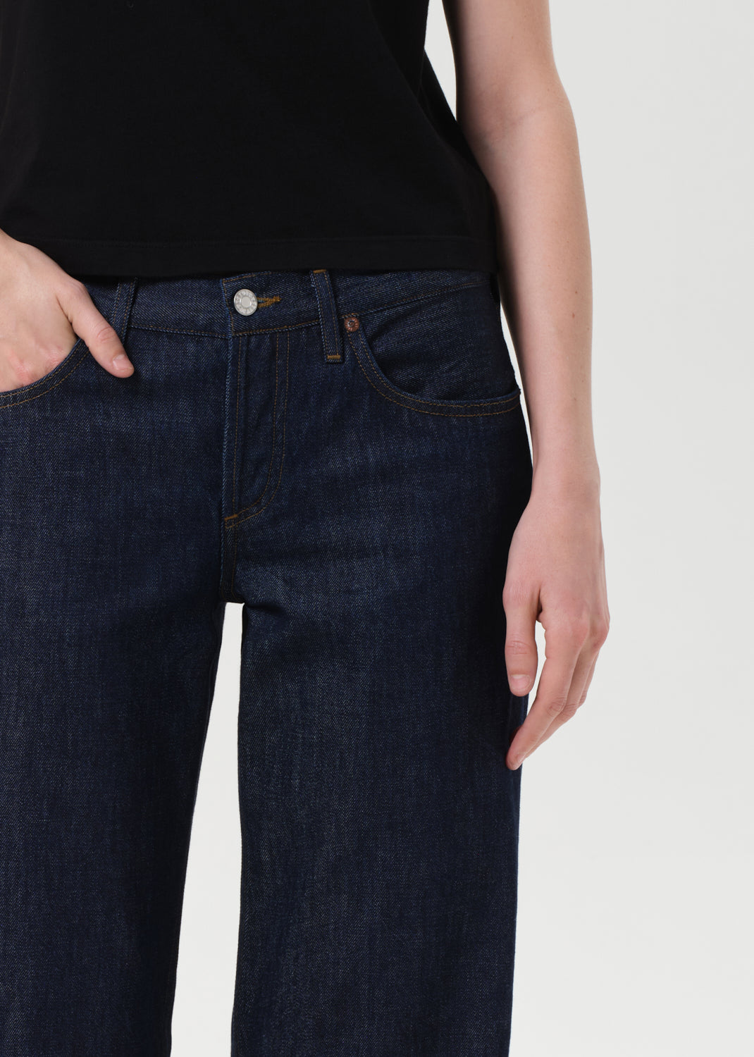 Person wearing dark blue jeans with a plain background
