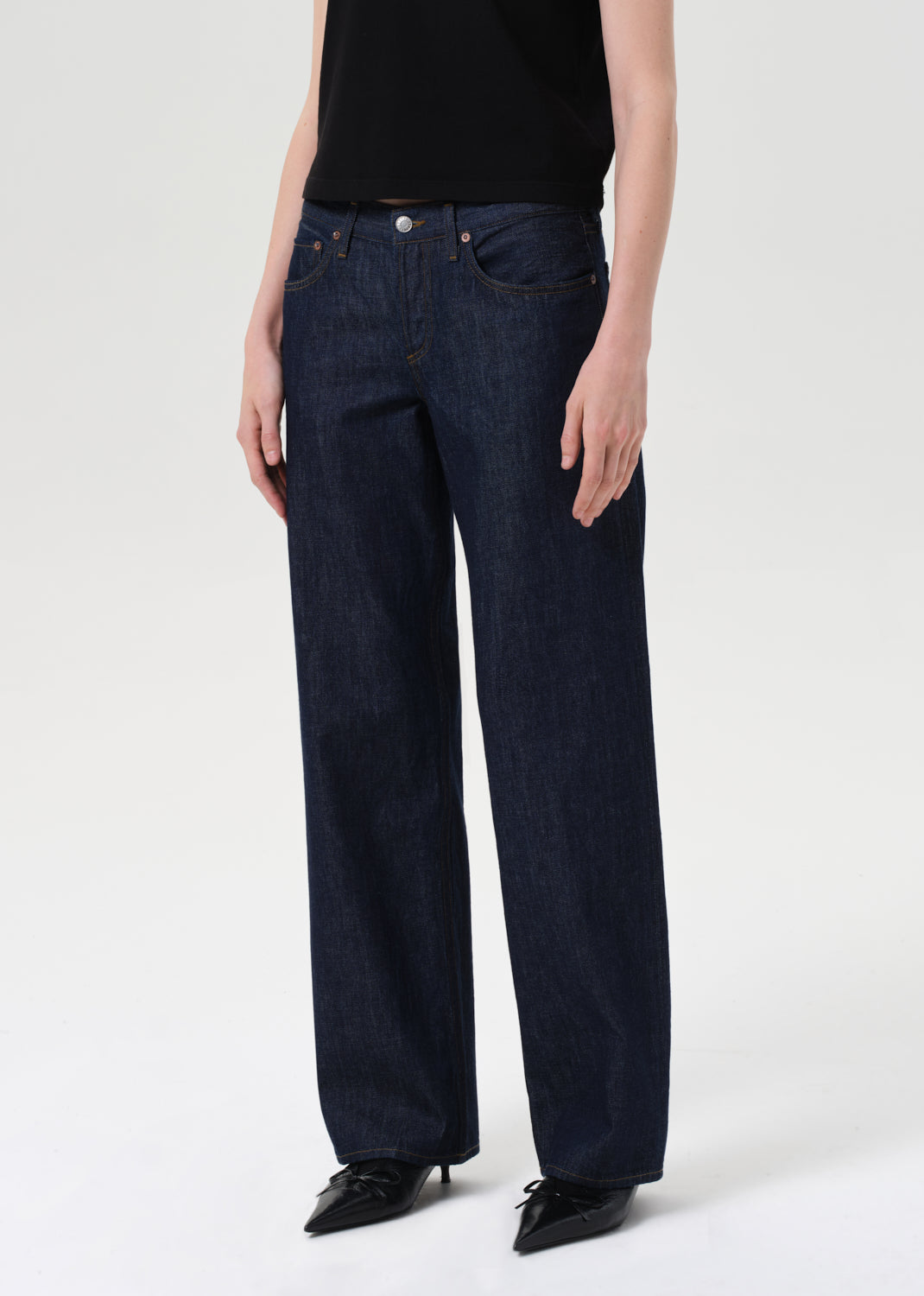 Person wearing dark blue jeans and black shoes on a white background