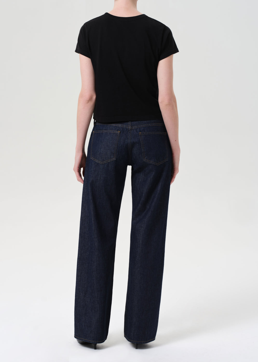 Person wearing a black t-shirt and dark blue jeans on a white background