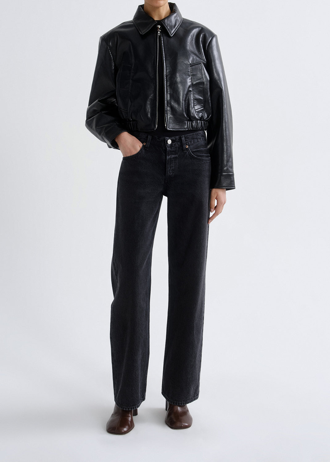 Person wearing a black leather jacket and black pants on a grey background