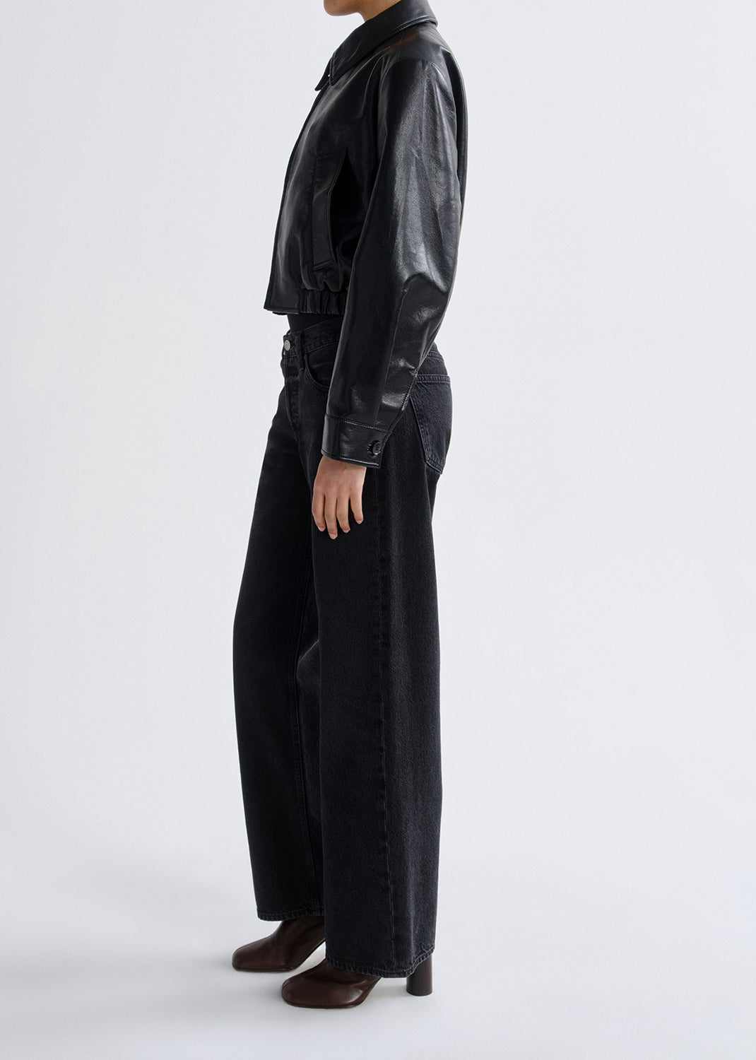 Person wearing a black leather jacket and pants on a grey background