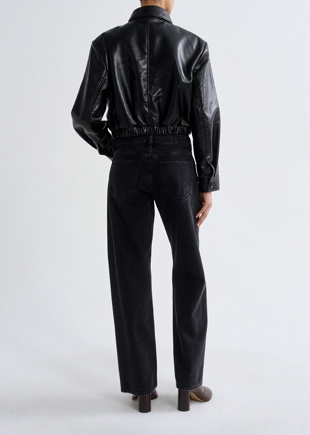 Person wearing a black leather jacket and black pants on a grey background