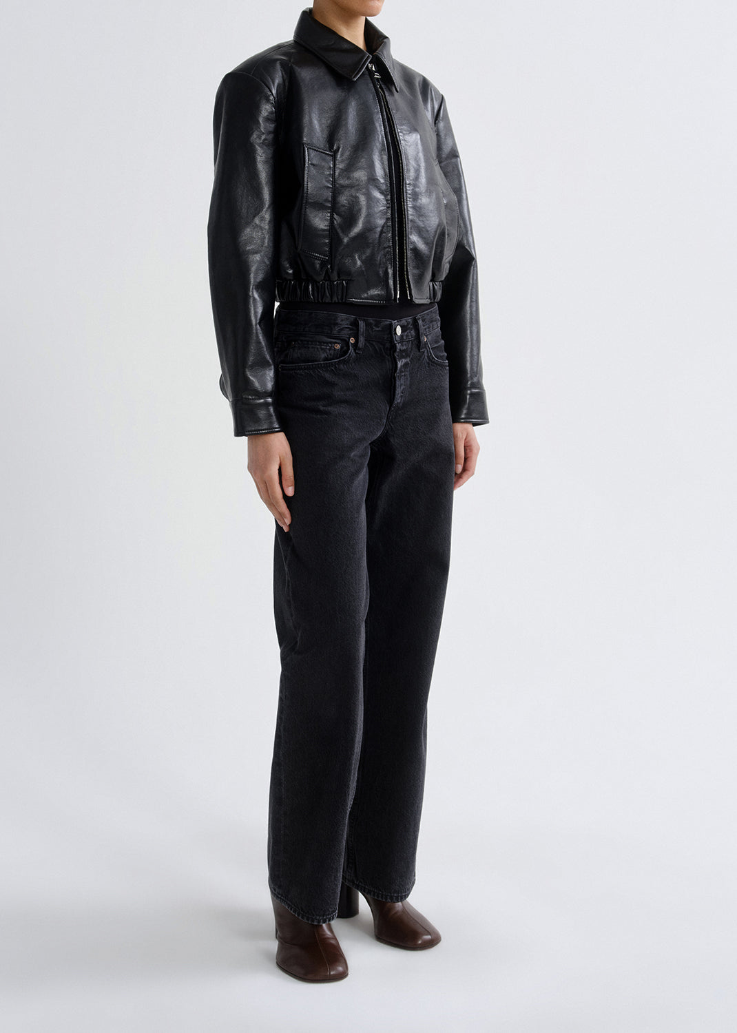 Person wearing a black leather jacket and pants on a grey background
