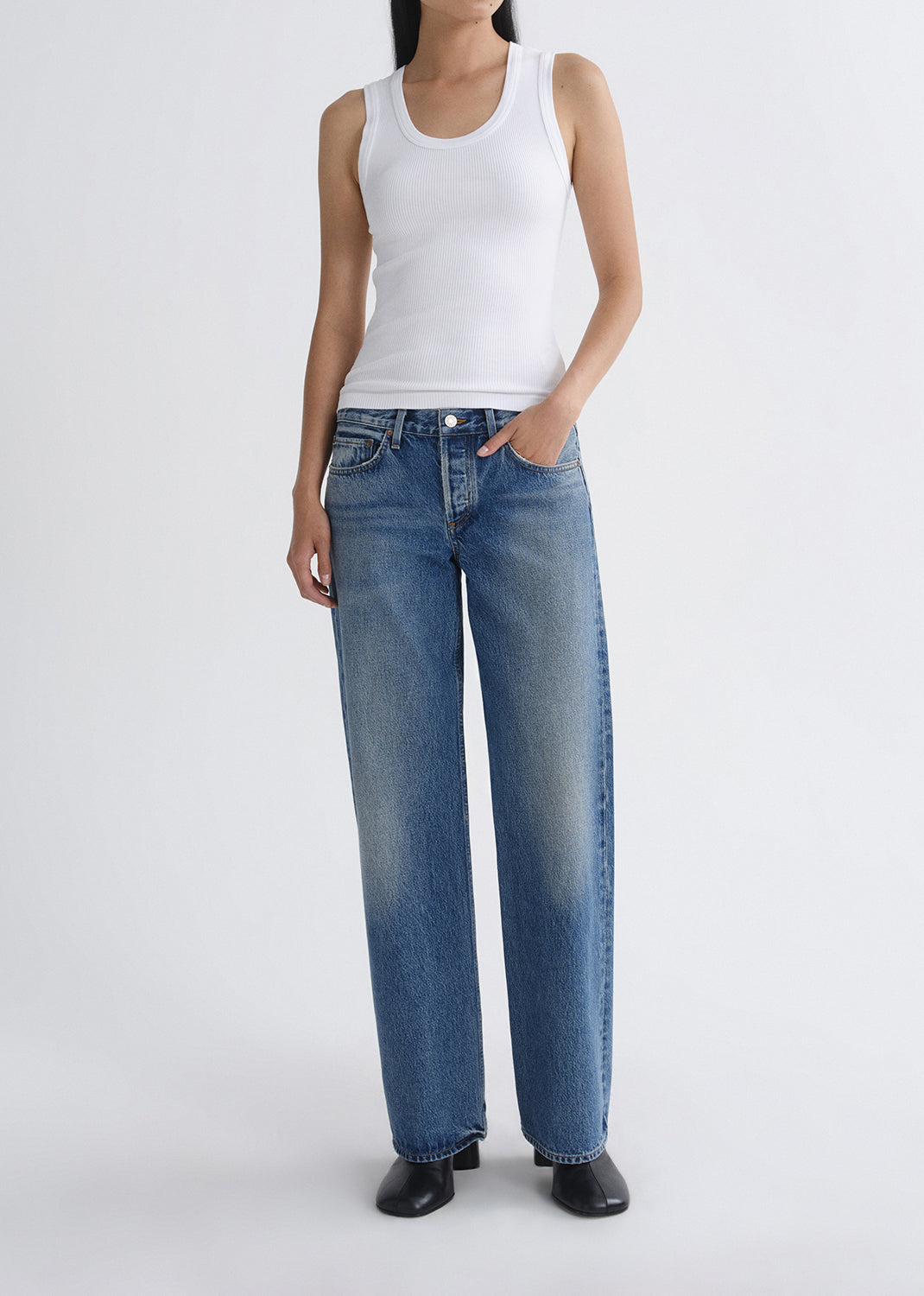 Person wearing a white tank top and blue jeans on a grey background