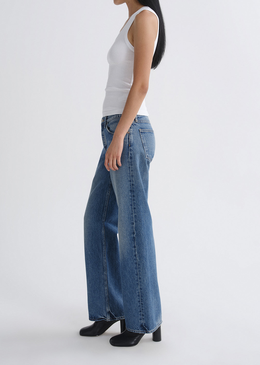 Person wearing blue jeans and a white top on a grey background