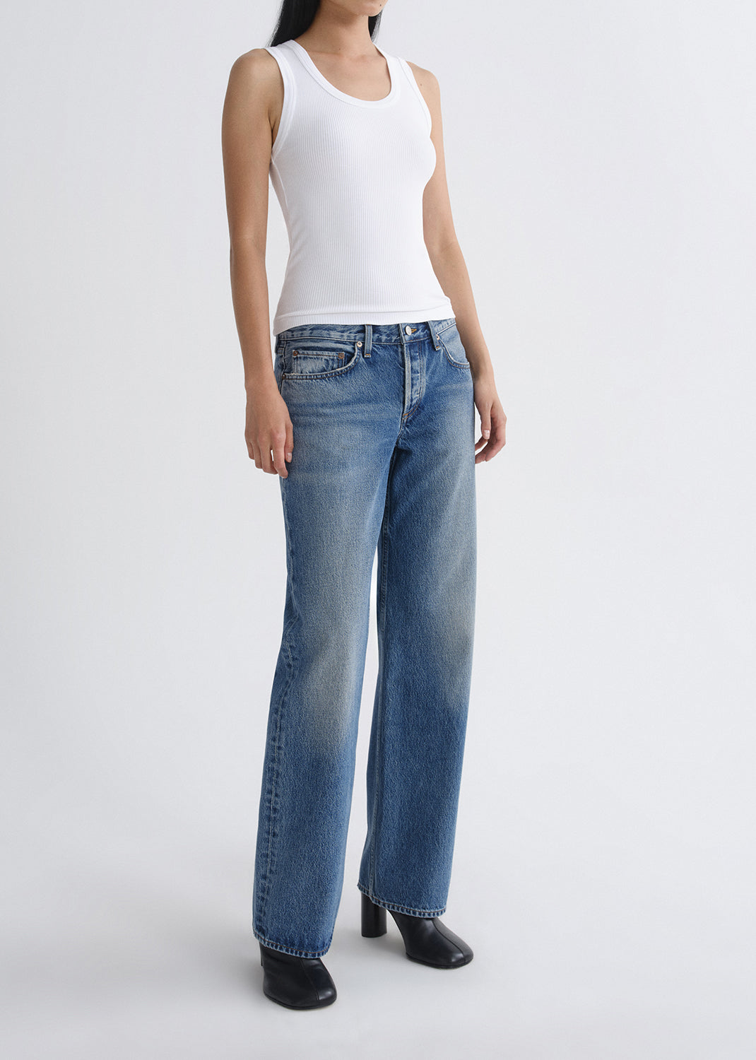 Person wearing a white tank top and blue jeans on a grey background