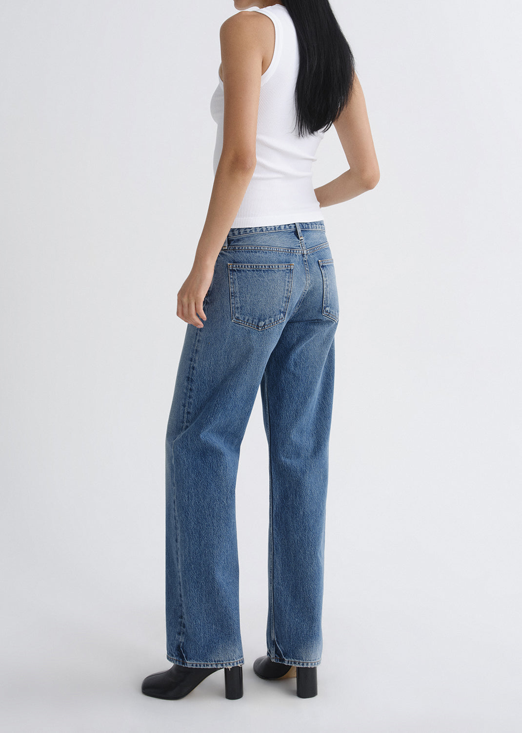 Person wearing blue jeans and a white top on a grey background