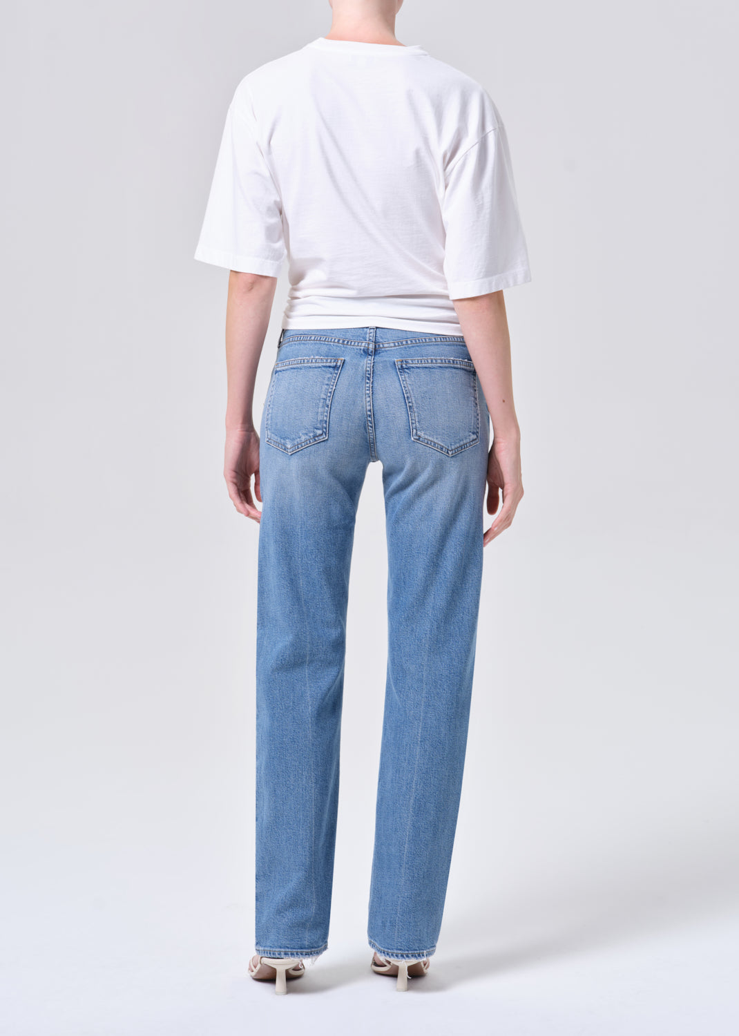 Person wearing a white t-shirt and blue jeans on a plain background