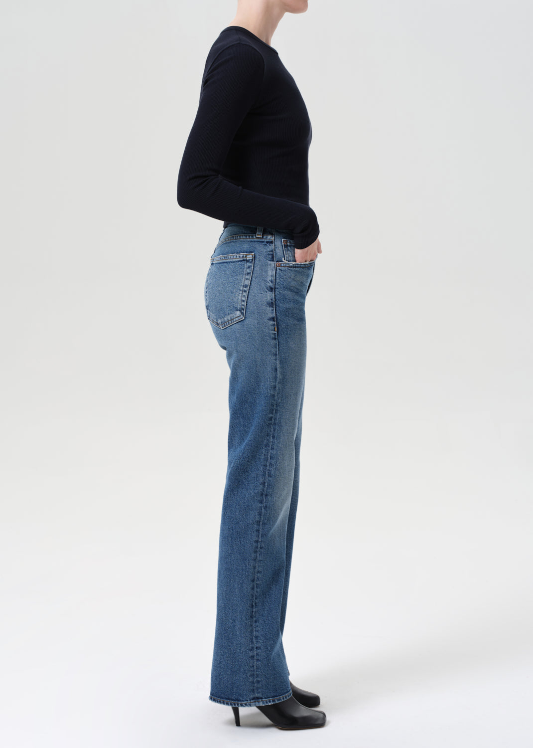 Person wearing blue jeans and a black top on a white background