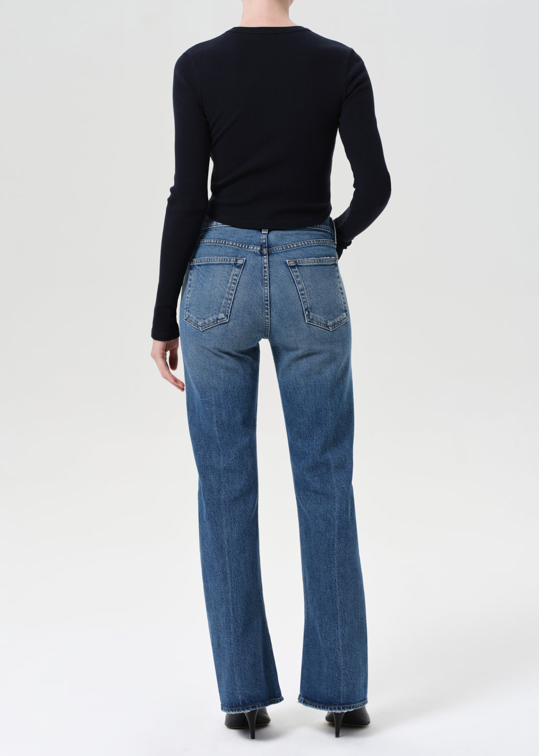 Person wearing blue jeans and a black top on a white background