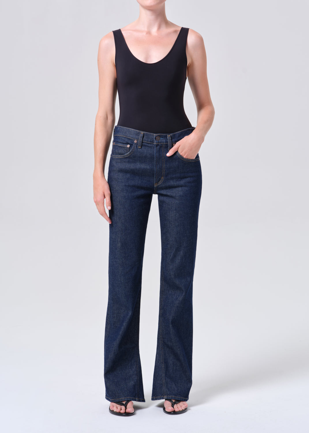 Person wearing a black sleeveless top and dark blue jeans on a white background