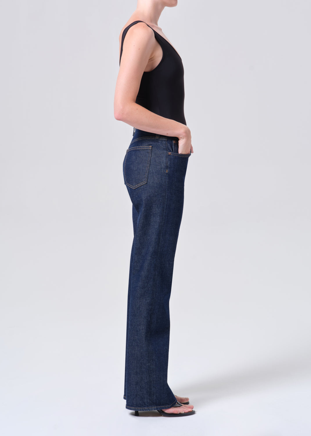 Person wearing dark blue jeans and a black tank top on a white background