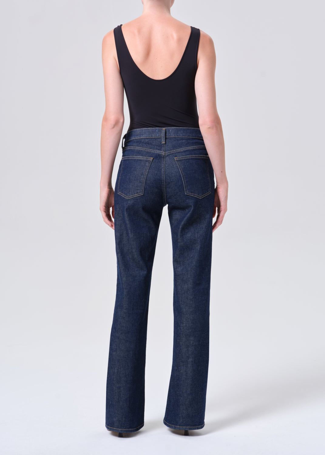 Person wearing dark blue jeans and a black tank top on a white background