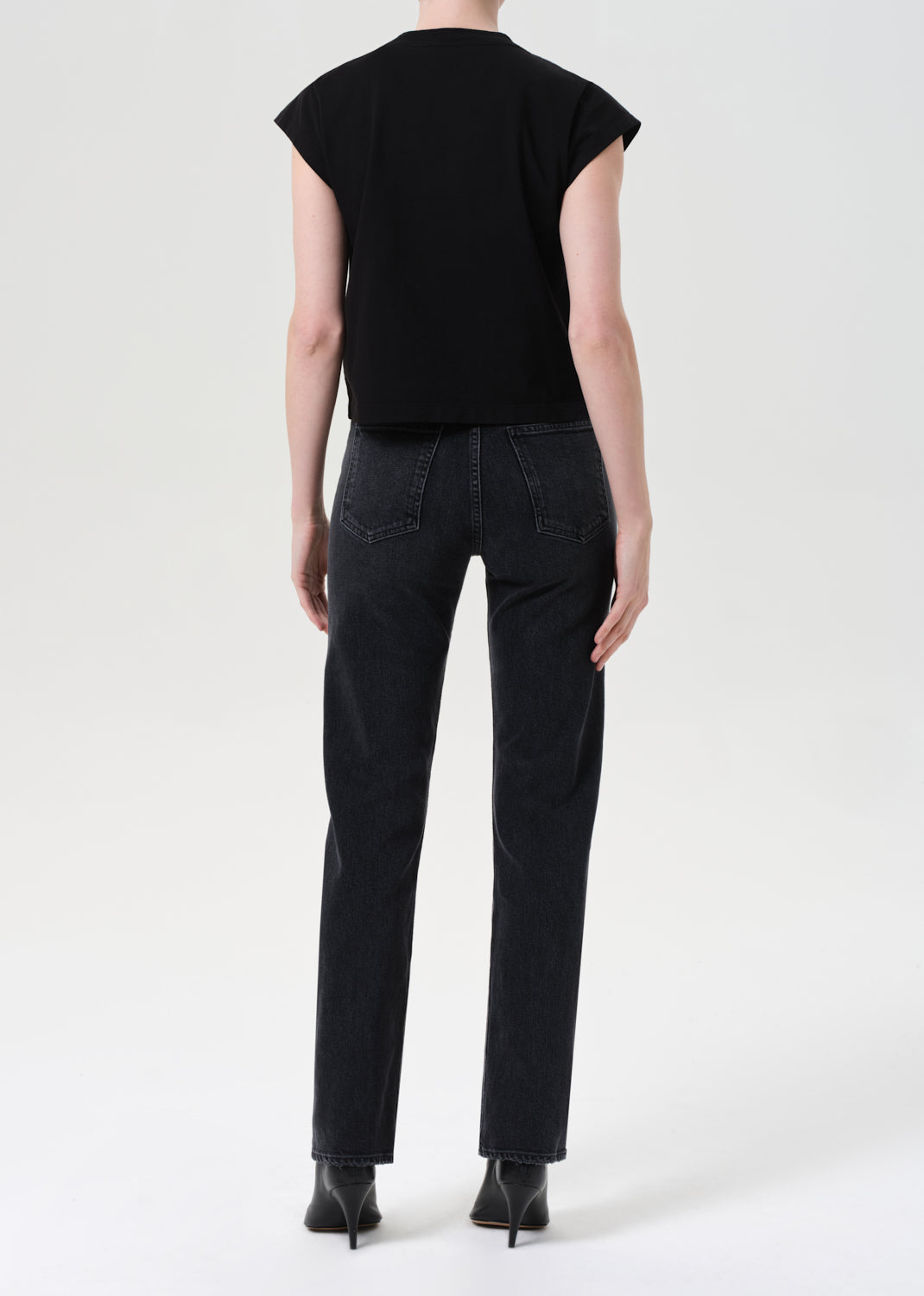 Person wearing a black sleeveless top and black jeans on a white background
