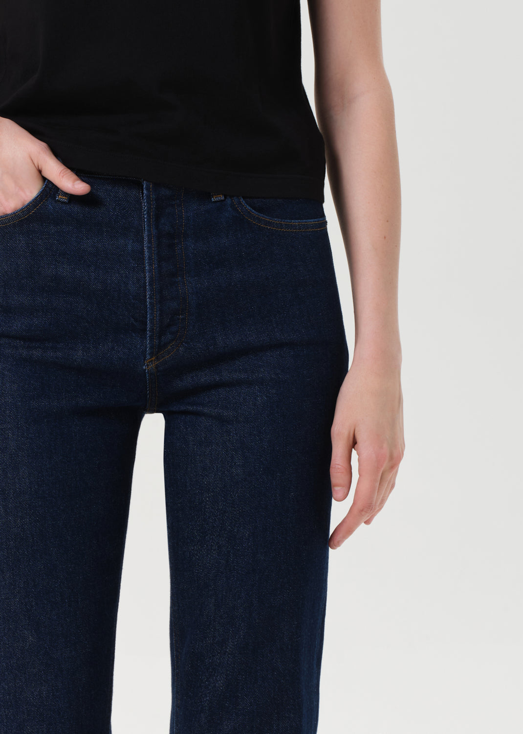 Person wearing dark blue jeans and a black top on a light gray background