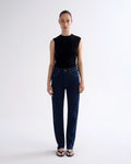 A model stands against a light gray studio background wearing a sleeveless black top and dark blue straight-leg jeans with black sandals.