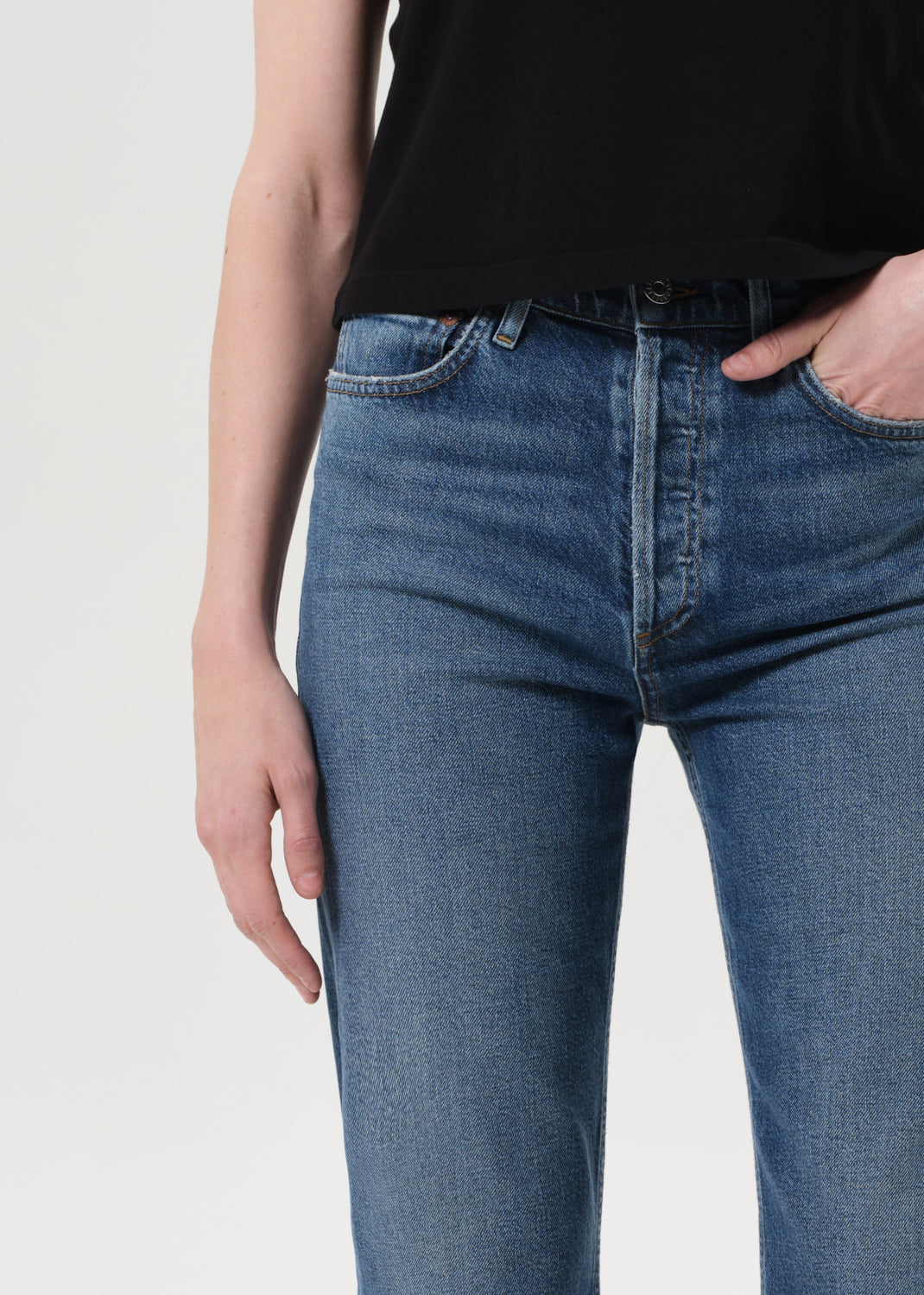 Person wearing blue jeans and a black top on a light gray background