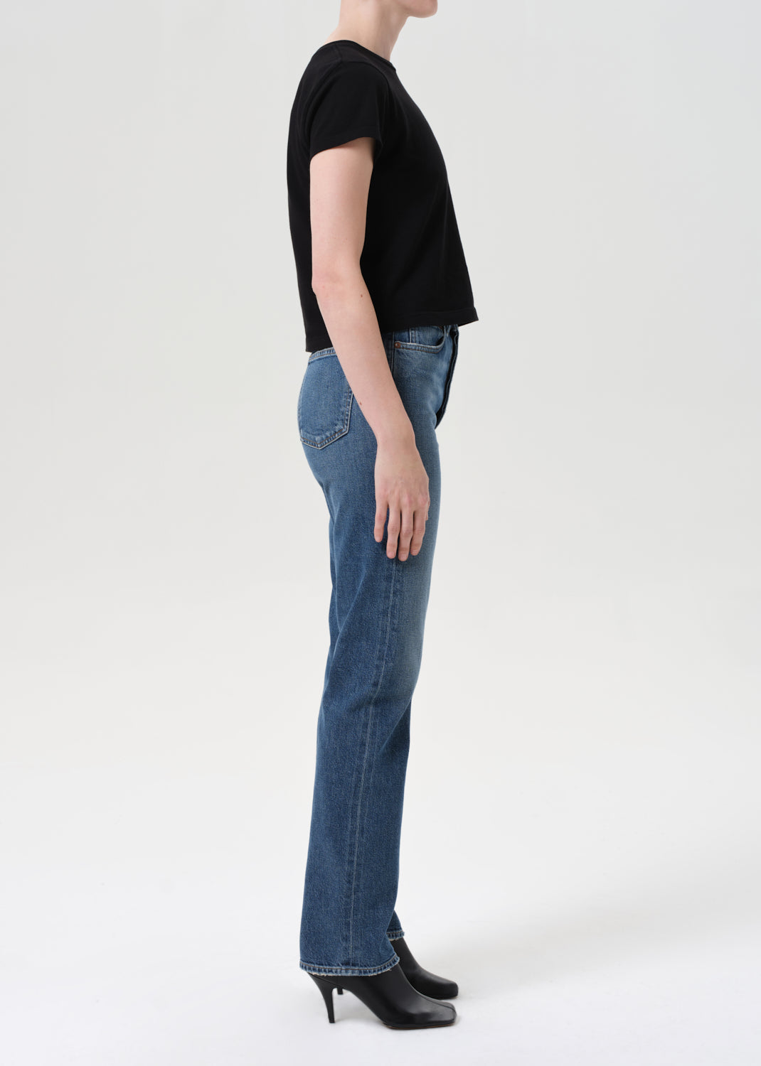 Person wearing blue jeans and a black top on a white background