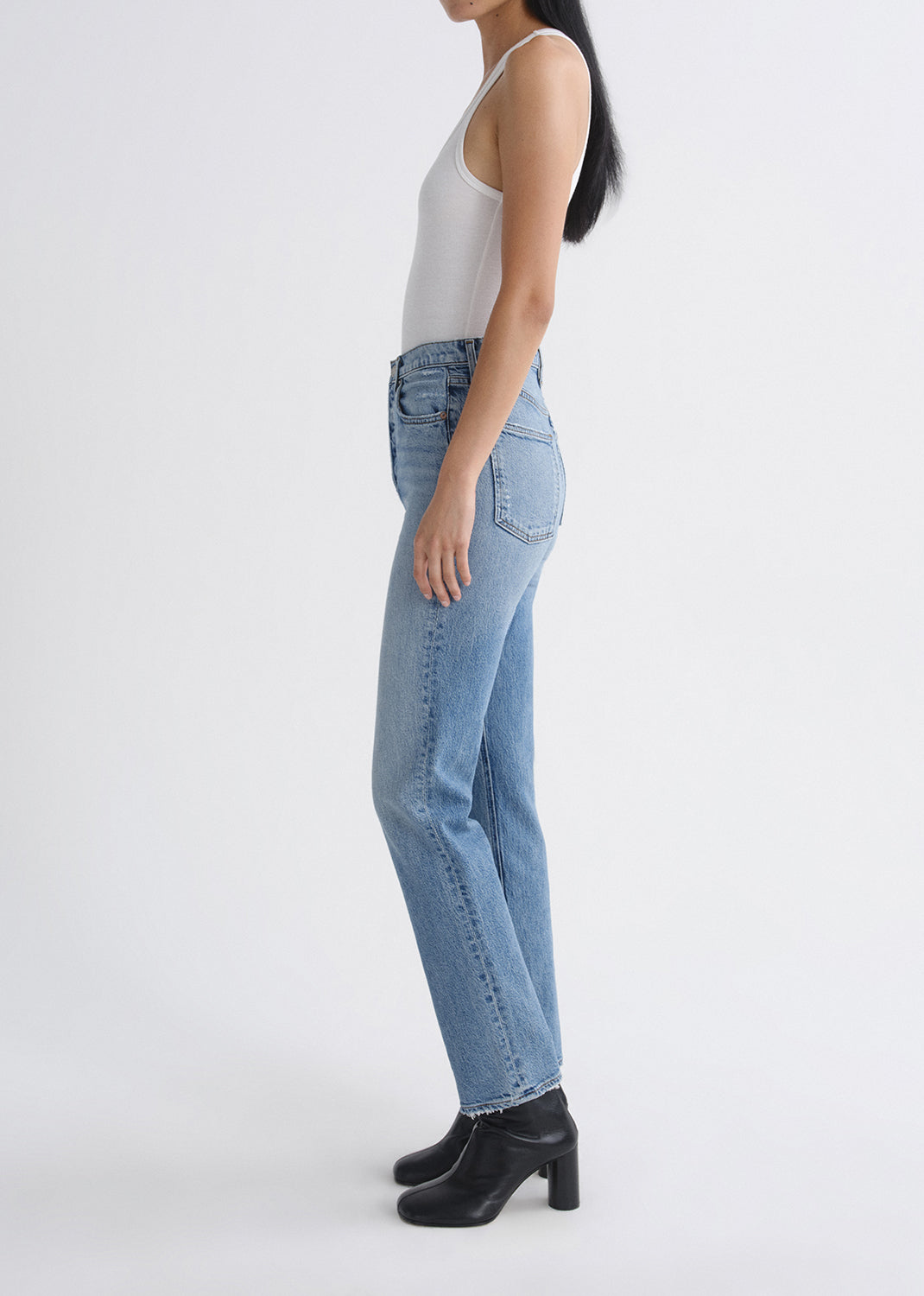 Person wearing light blue jeans and a white top on a grey background
