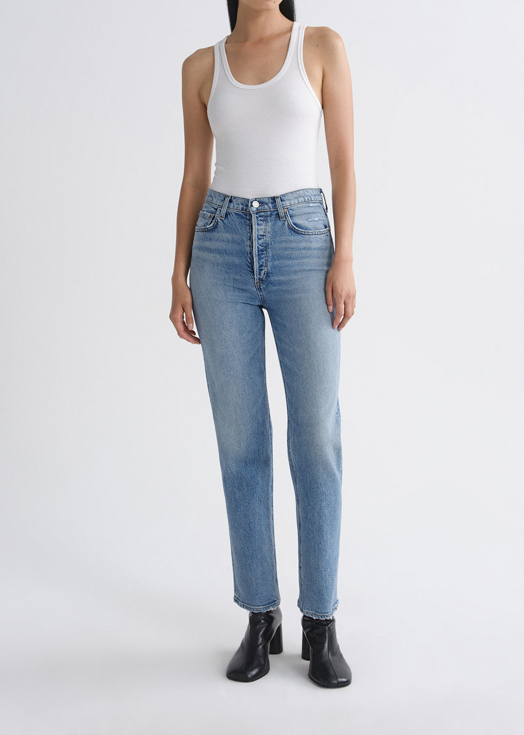 Person wearing light blue jeans and a white tank top on a grey background