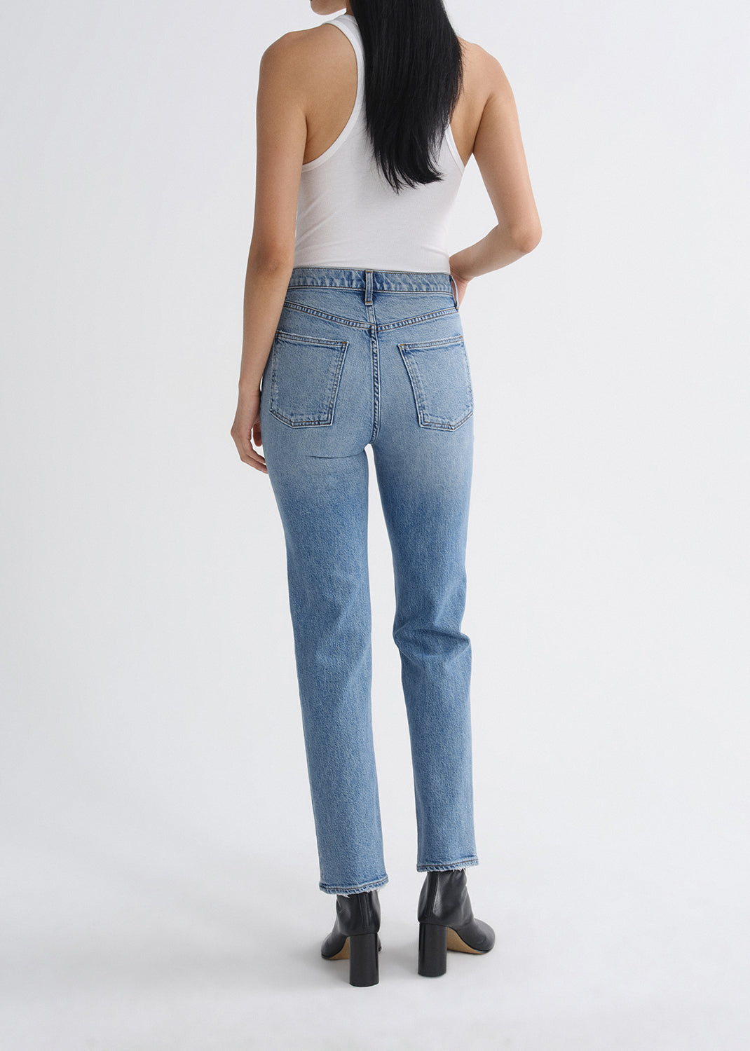 Back of person wearing light blue jeans and a white tank top on a grey background