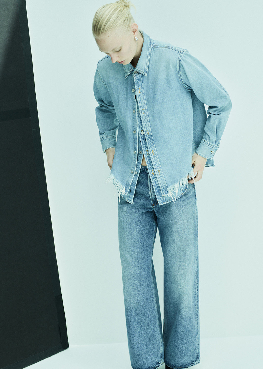 Person wearing a light blue denim jacket and jeans against a plain background