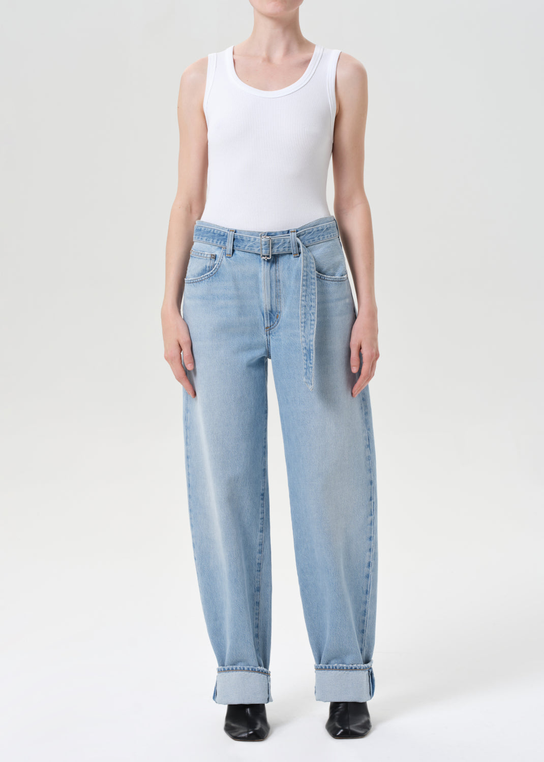 Person wearing light blue jeans and a white tank top on a white background