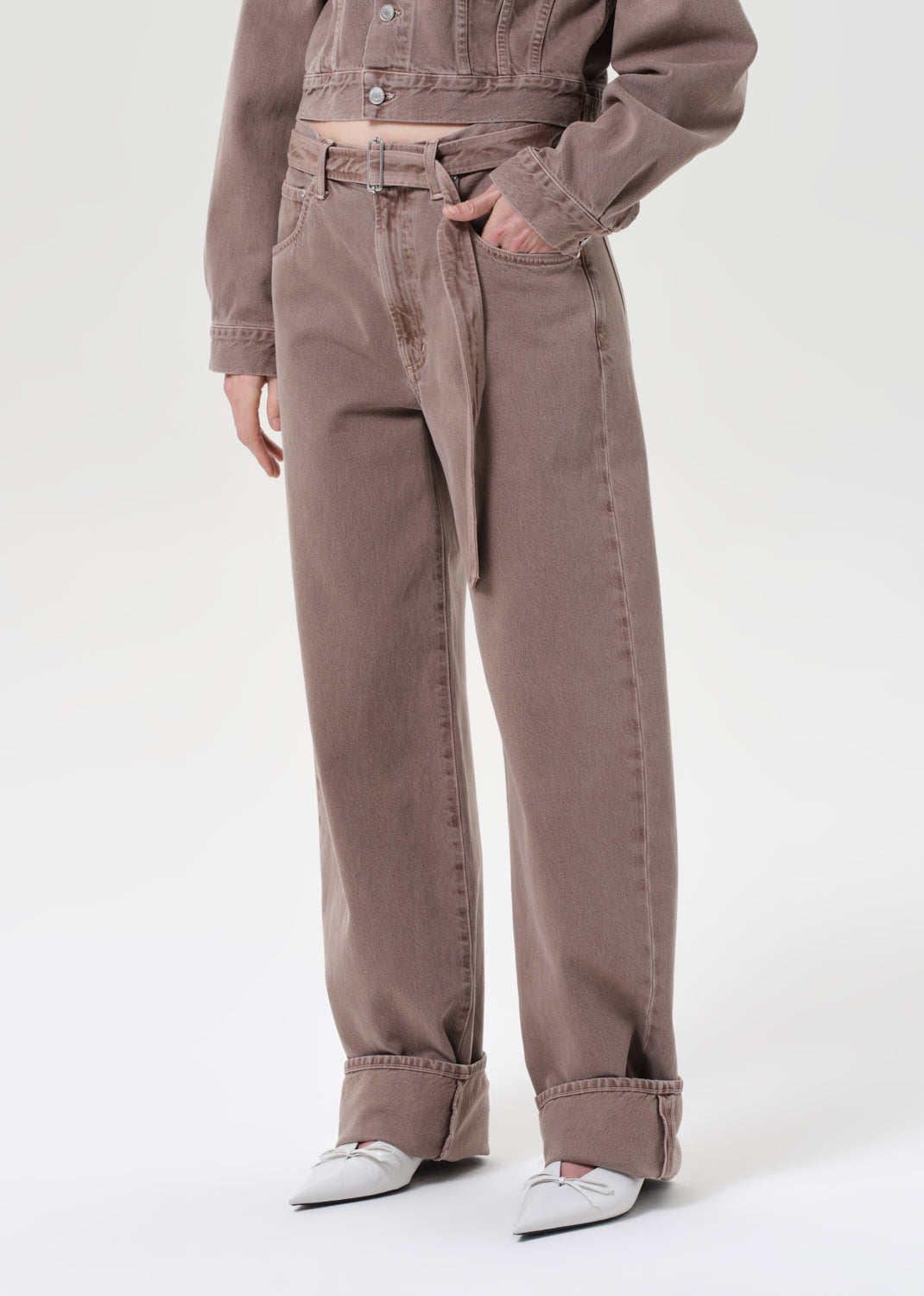 Person wearing a brown jacket and pants with white shoes on a white background