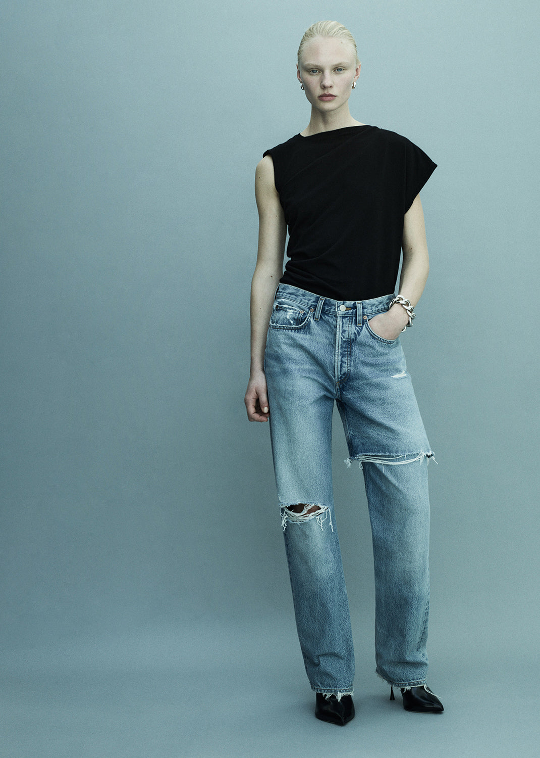 Person wearing a black top and light blue jeans on a gray background