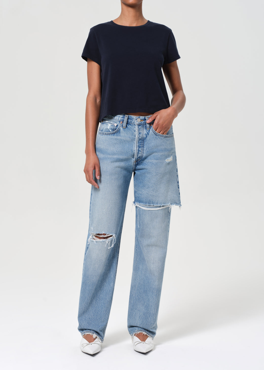 Person wearing a black t-shirt and light blue jeans with distressing on a white background