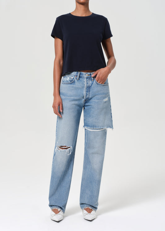 Person wearing a black t-shirt and light blue jeans with distressing on a white background