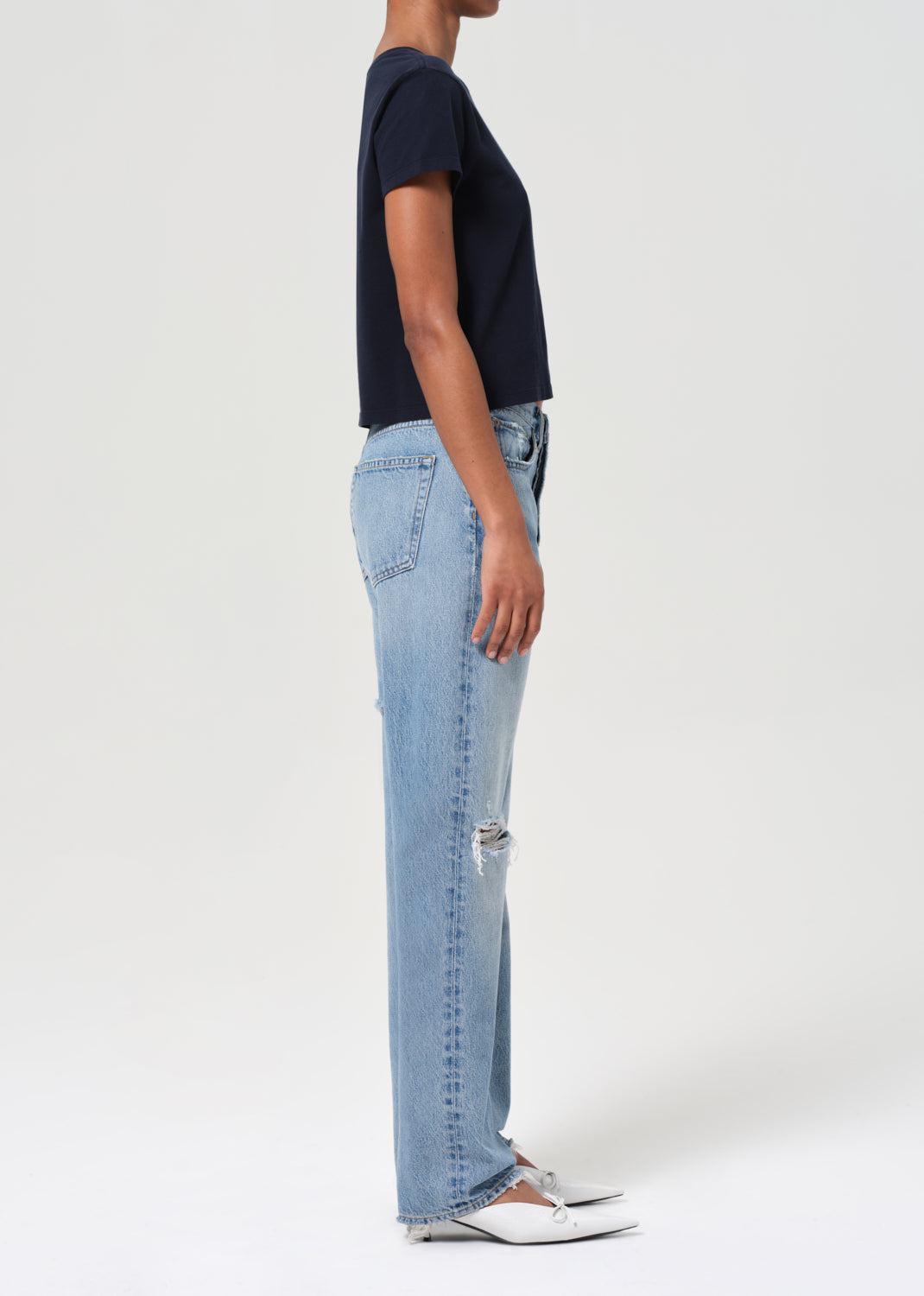 Person wearing light blue jeans and a dark top on a white background