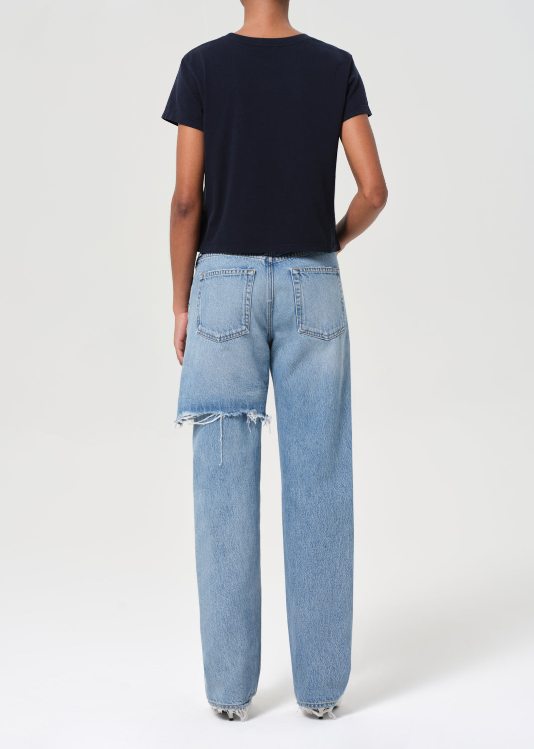 Person wearing a navy t-shirt and light blue jeans on a white background