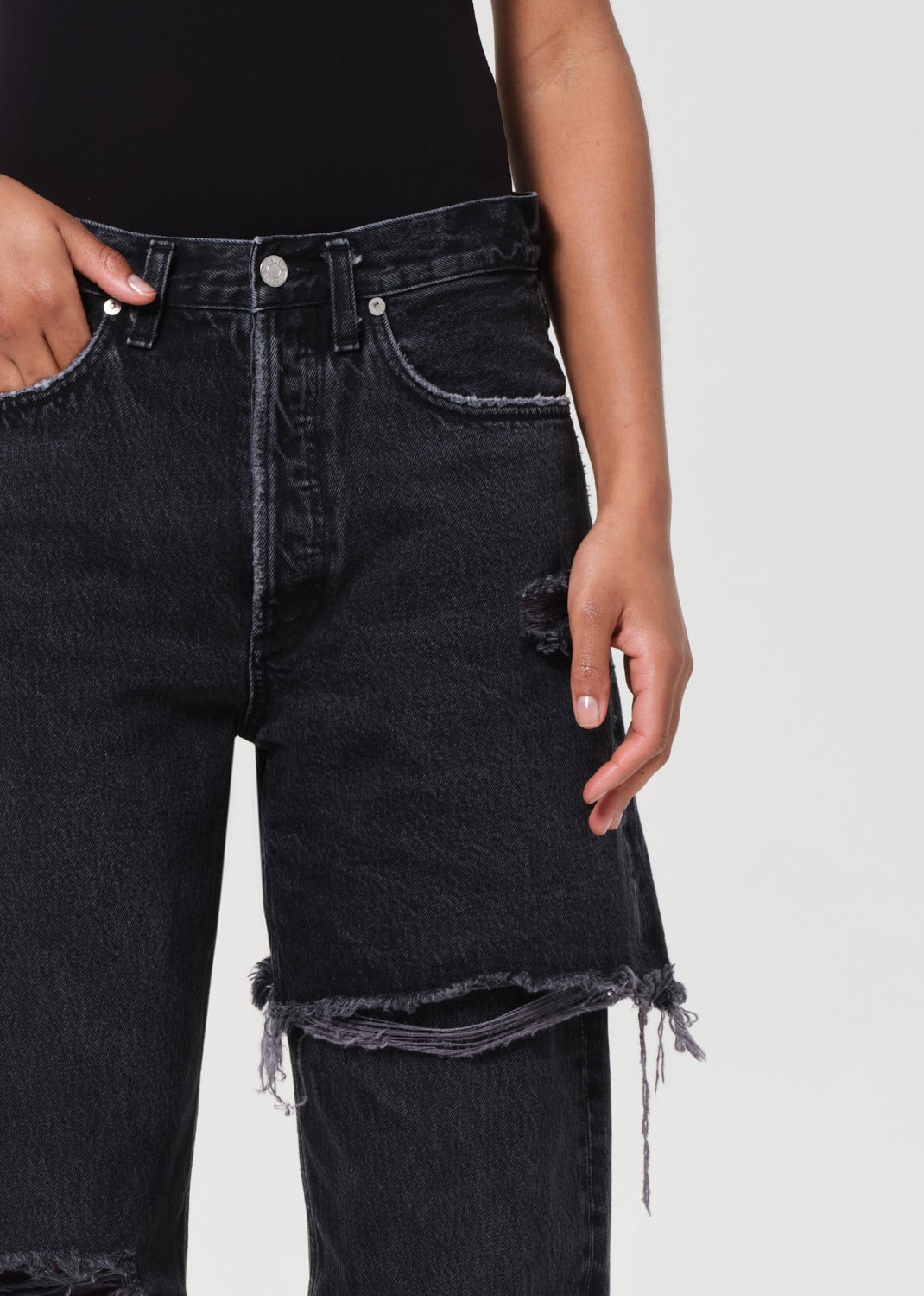 Black distressed jeans worn by a person on a white background