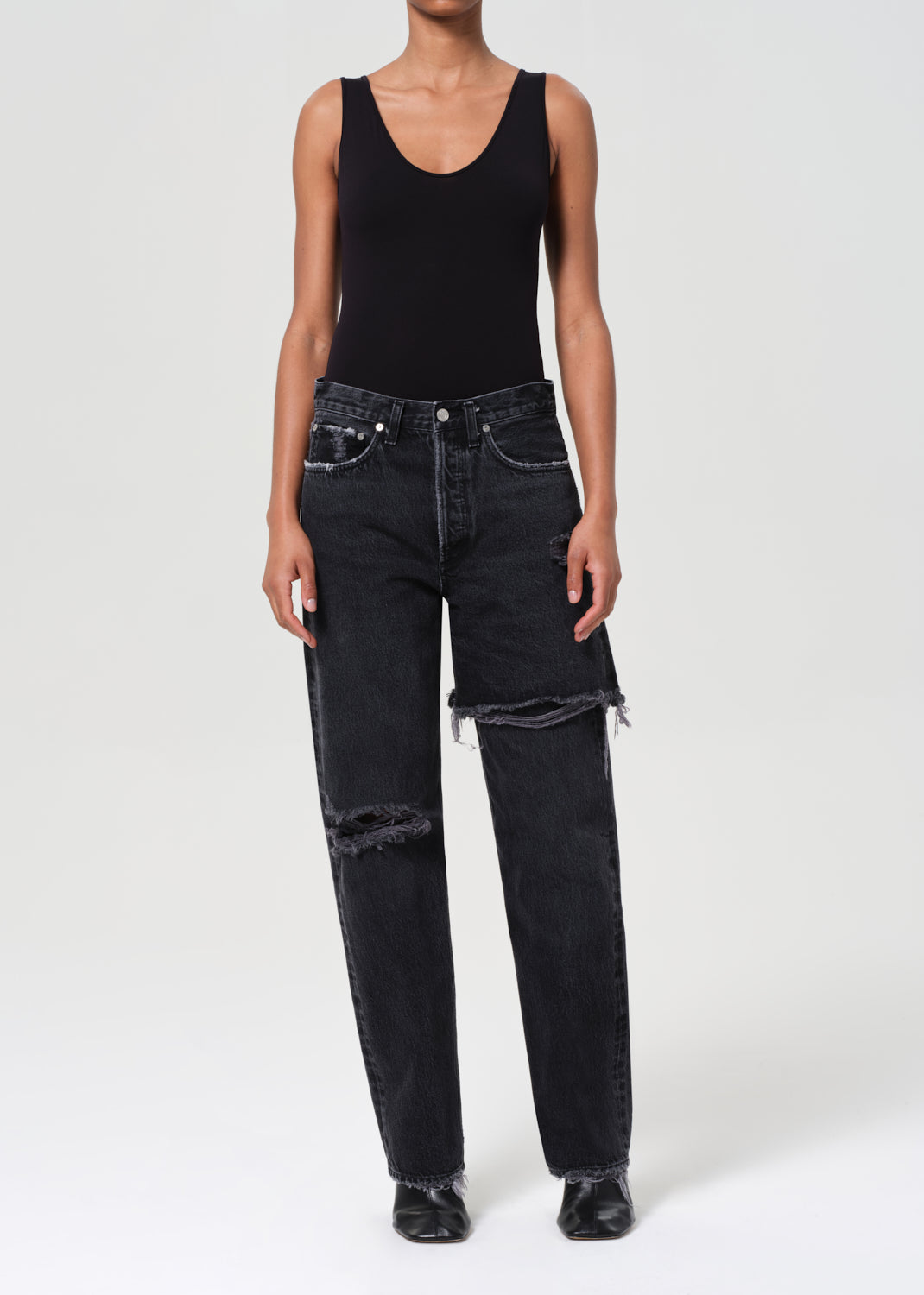 Person wearing a black tank top and black distressed jeans on a white background