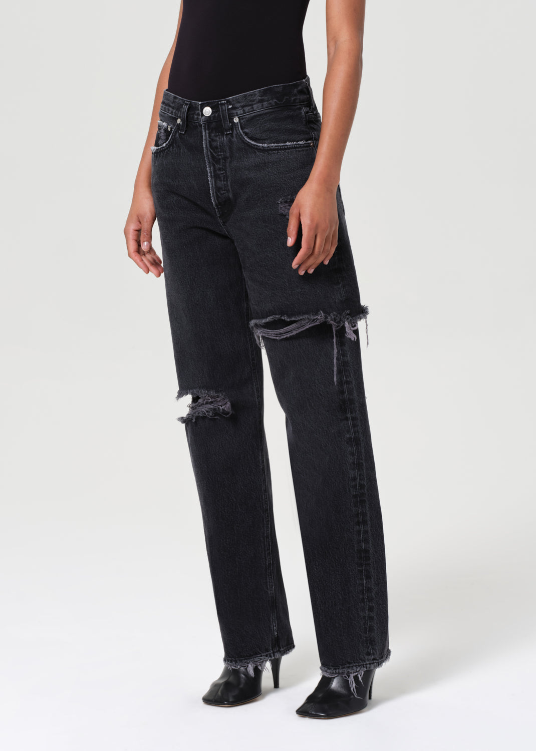 Person wearing black distressed jeans on a white background
