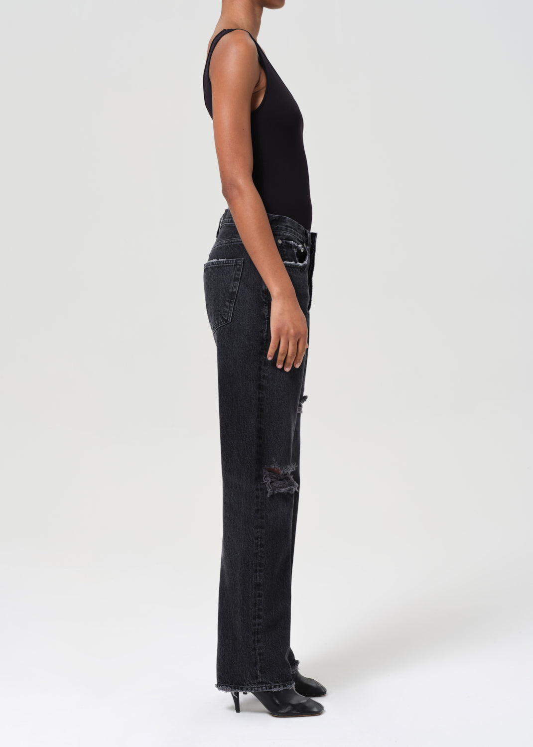 Person wearing black distressed jeans and a black sleeveless top on a white background