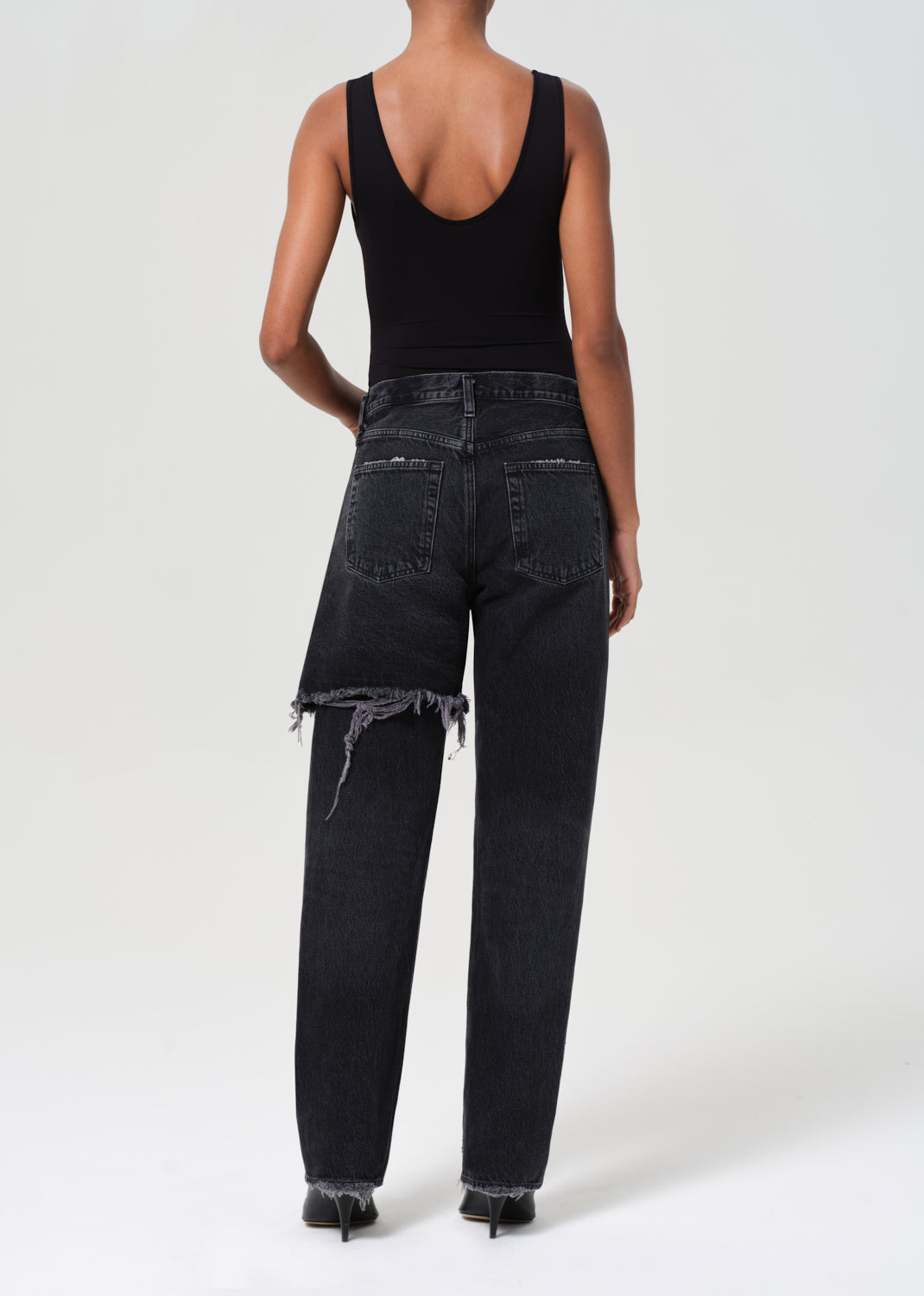 Person wearing black distressed jeans and a black tank top on a white background