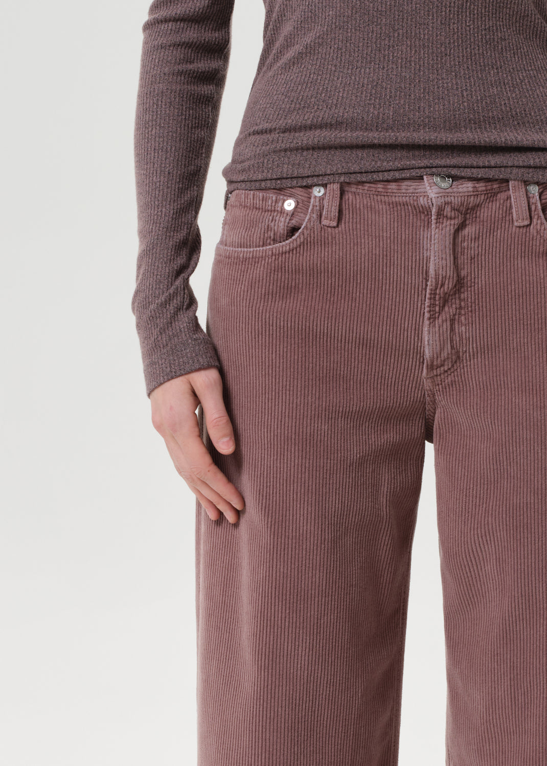 Person wearing brown ribbed long-sleeve shirt and corduroy pants on a light gray background