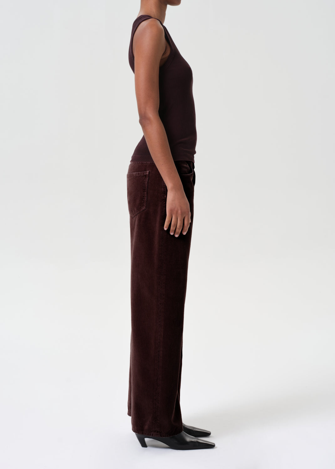 Person wearing a brown sleeveless top and wide-leg pants on a white background