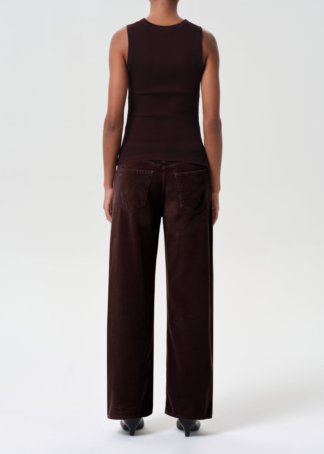 Person wearing a brown sleeveless top and wide-leg pants on a white background