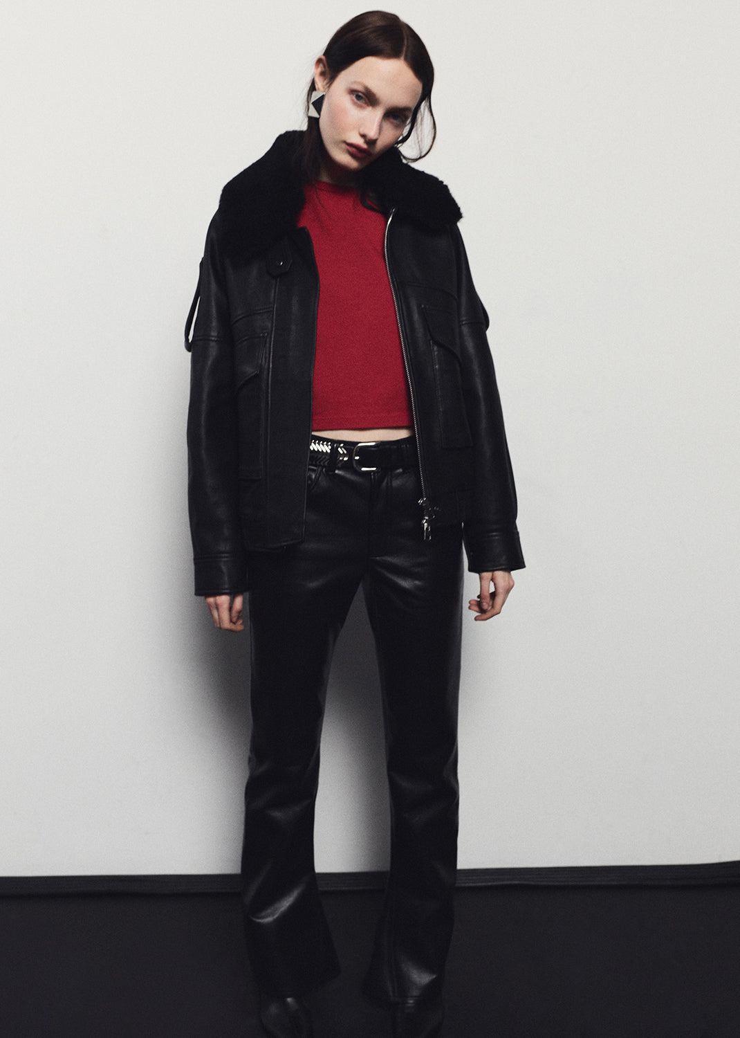 Person wearing a black leather jacket and pants with a red top against a white background