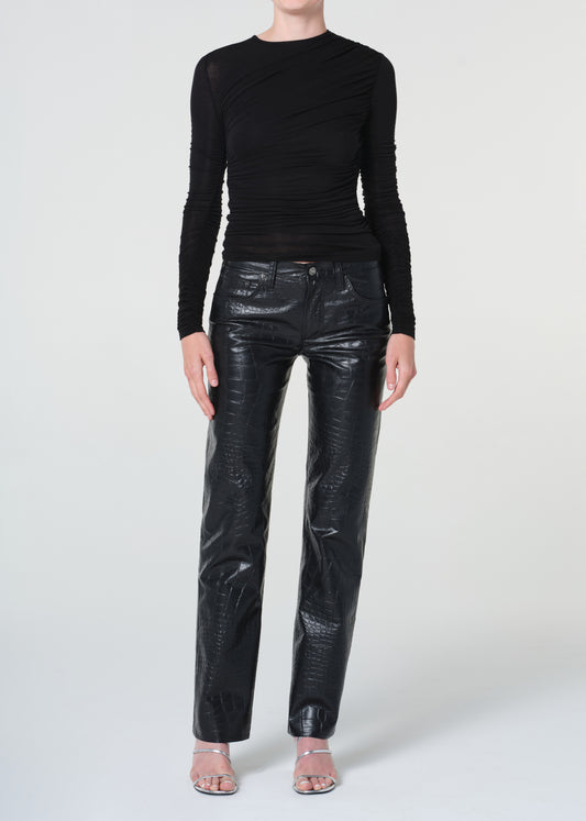 Person wearing a black long-sleeve top and shiny black pants on a white background