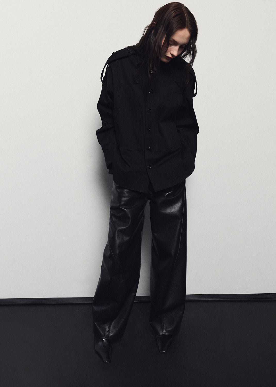 Person wearing a black outfit with wide-leg pants against a white wall.