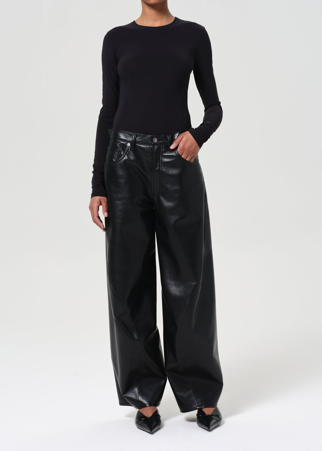 Person wearing a black long-sleeve top and black leather pants on a white background