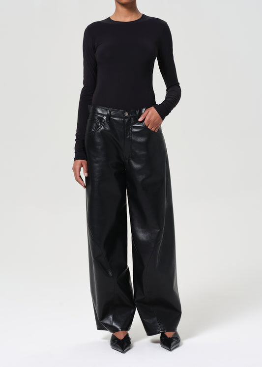 Person wearing a black long-sleeve top and black leather pants on a white background