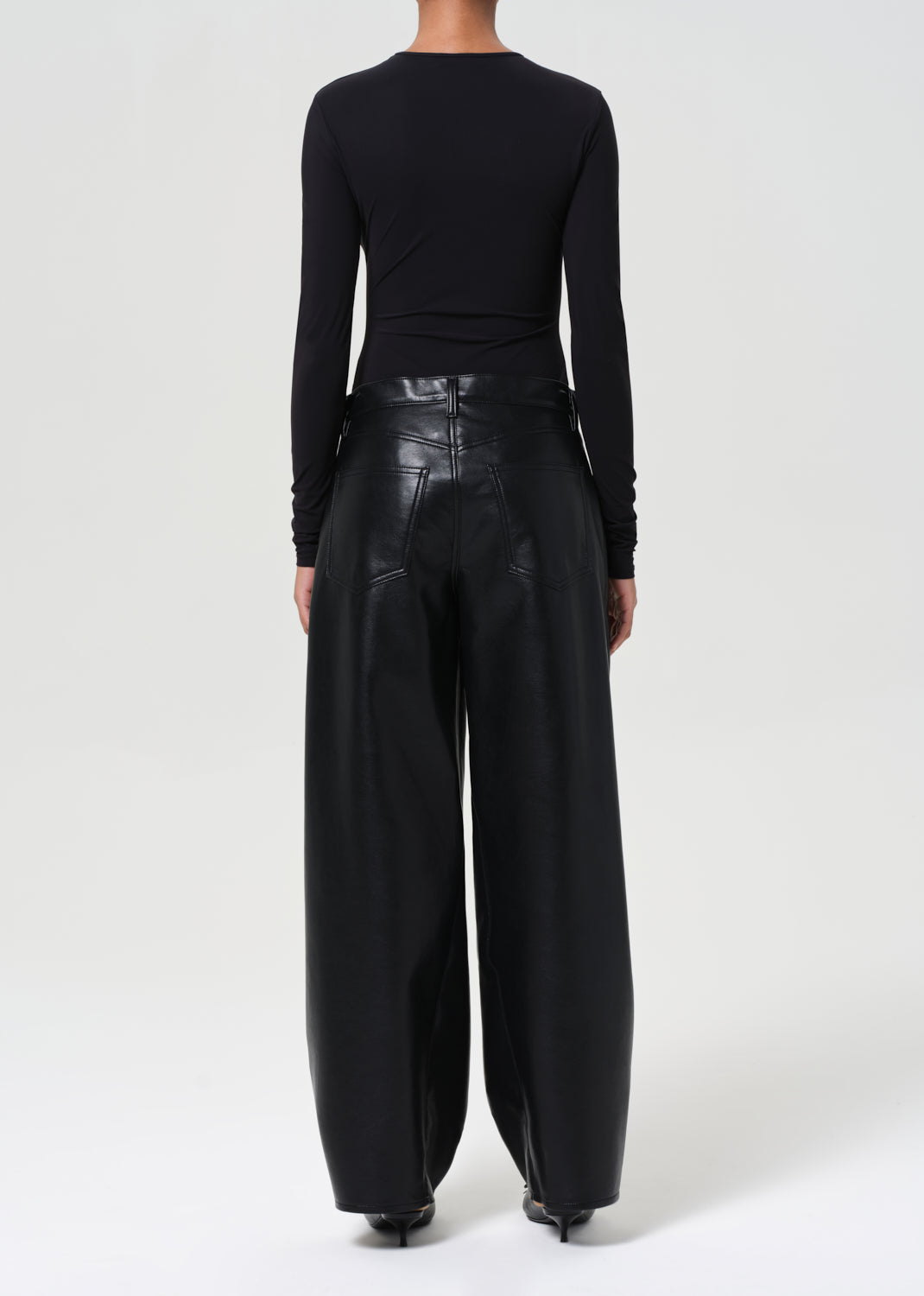 Person wearing a black long-sleeve top and black leather pants on a white background