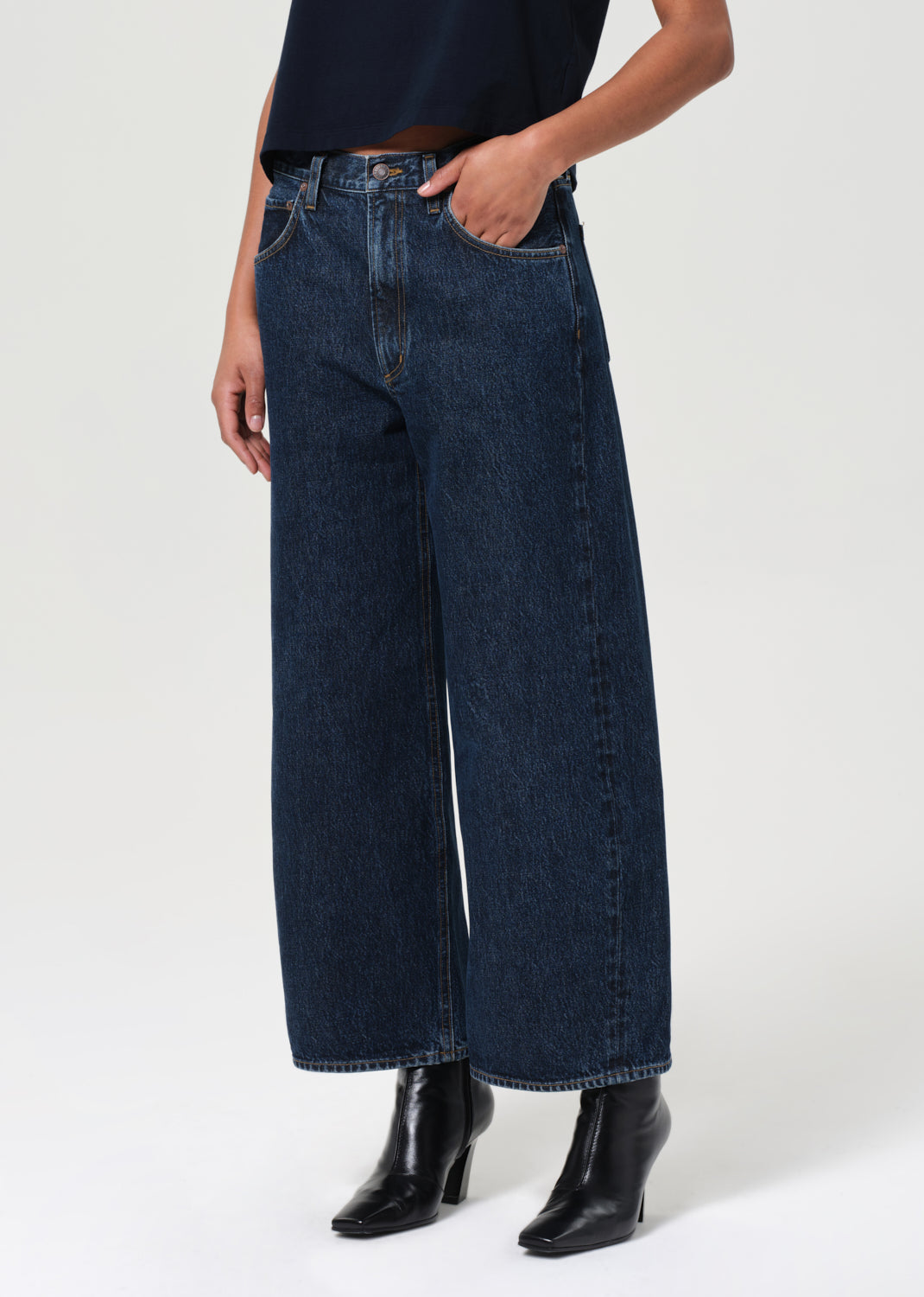 Person wearing dark blue wide-leg jeans and black shoes on a white background