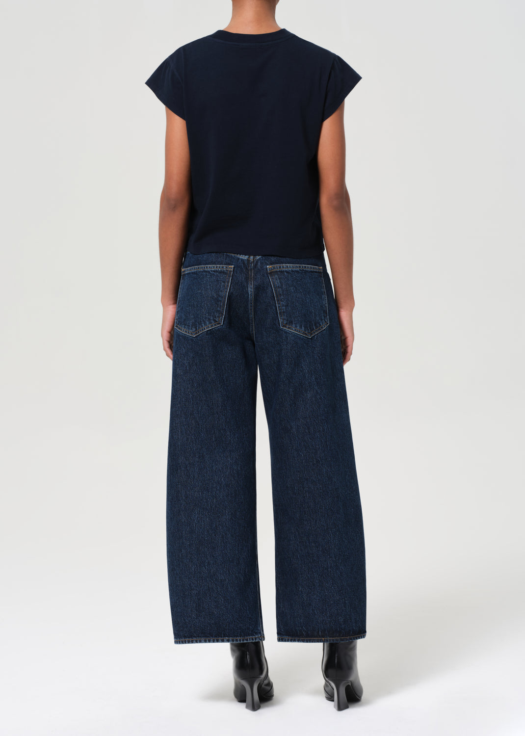 Person wearing a black top and dark blue jeans on a white background